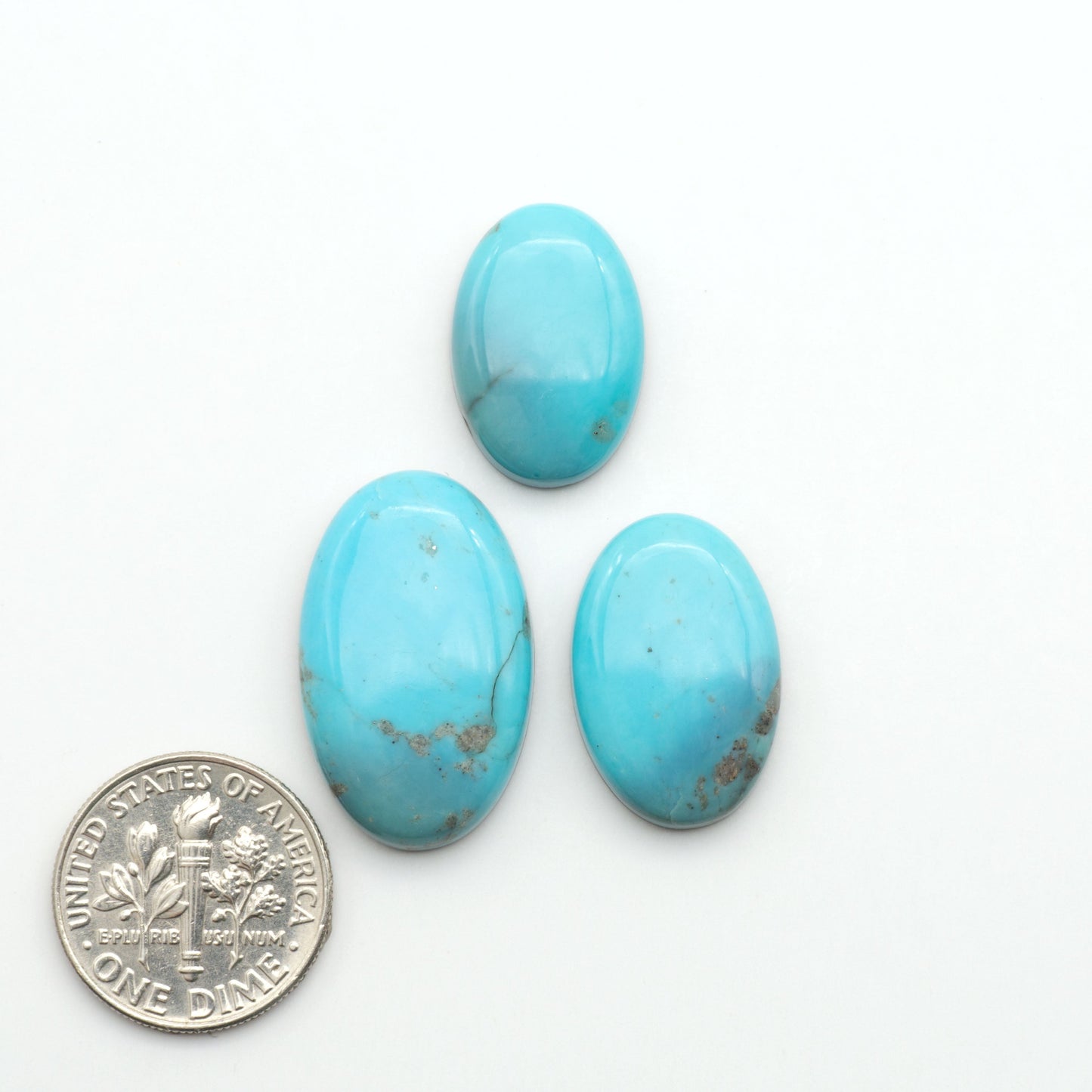 Three turquoise stones with a U.S. dime for scale on a white background