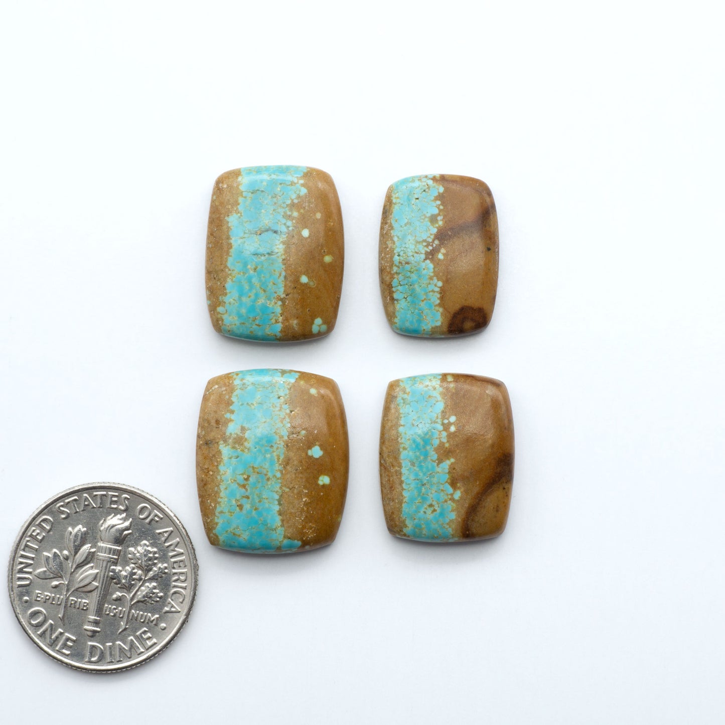 Four rectangular beads with turquoise stripes next to a dime on a white background. Number 8 Turquoise Cabochons have been selected for their quality and unique appearance. Don't miss the chance to add a one-of-a-kind piece to your collection.