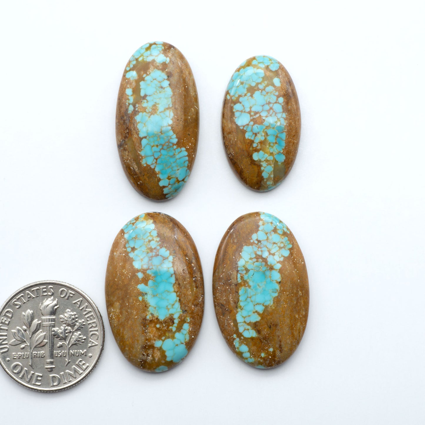 Four oval turquoise stones with brown matrix on a white background, one dollar coin for scale. Number 8 Turquoise Cabochons have been selected for their quality and unique appearance. Don't miss the chance to add a one-of-a-kind piece to your collection.