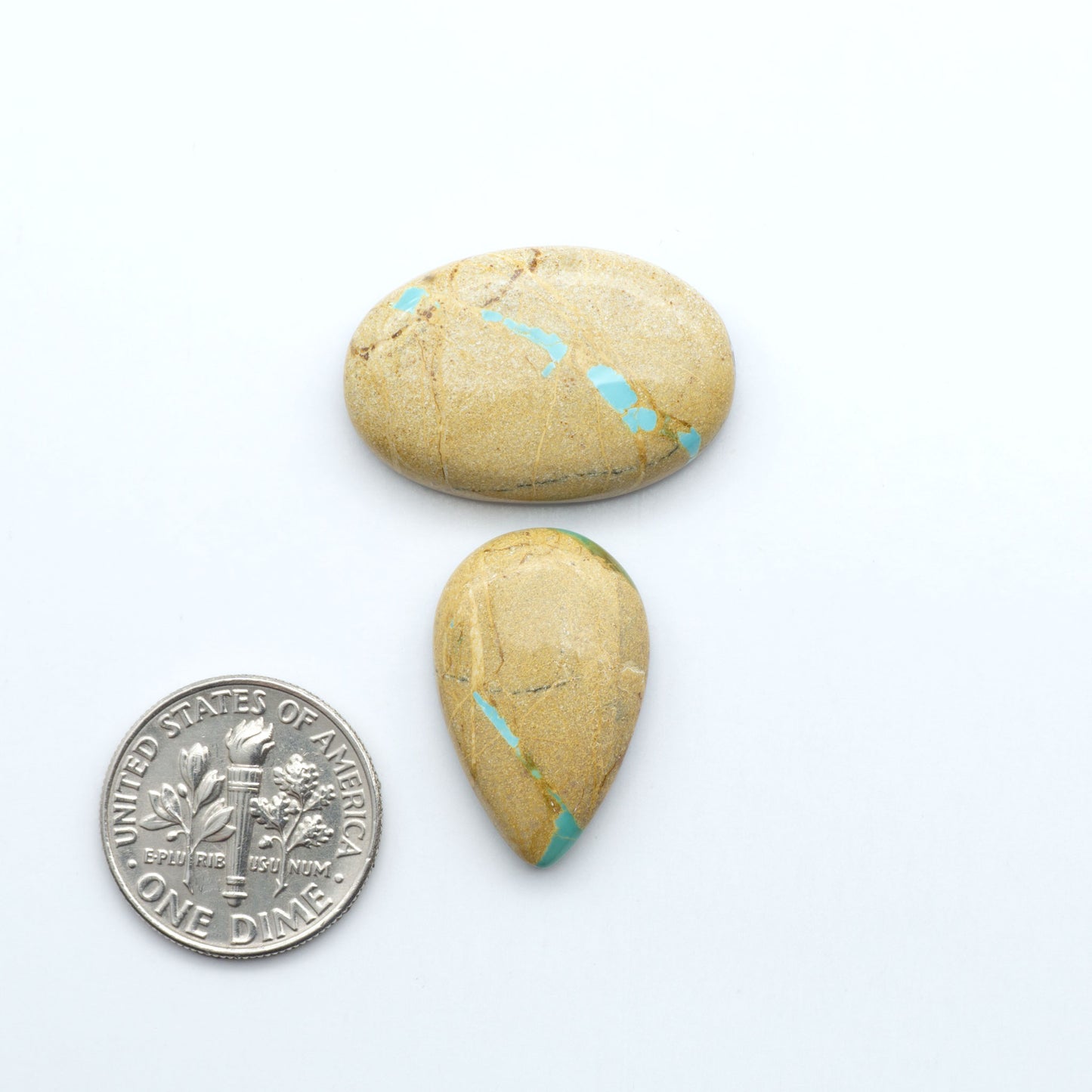 Two turquoise-stained stones next to a U.S. dime on a white background. Royston Turquoise cabochons are famous for their distinctive matrix and unique green and blue hues, making them a favored option among jewelry designers.