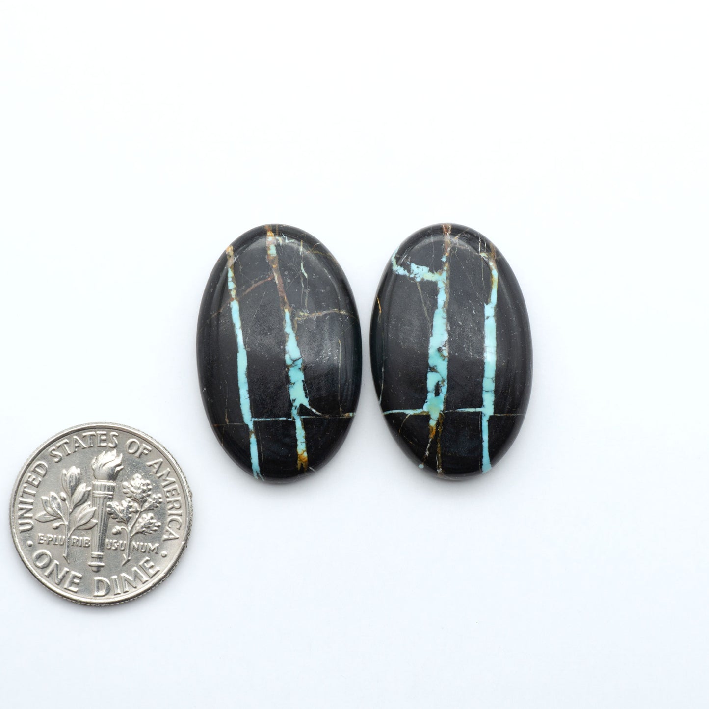 Black Jack turquoise cabochons, blue-green color with black matrix, polished stones on a white background with a US dime for scale