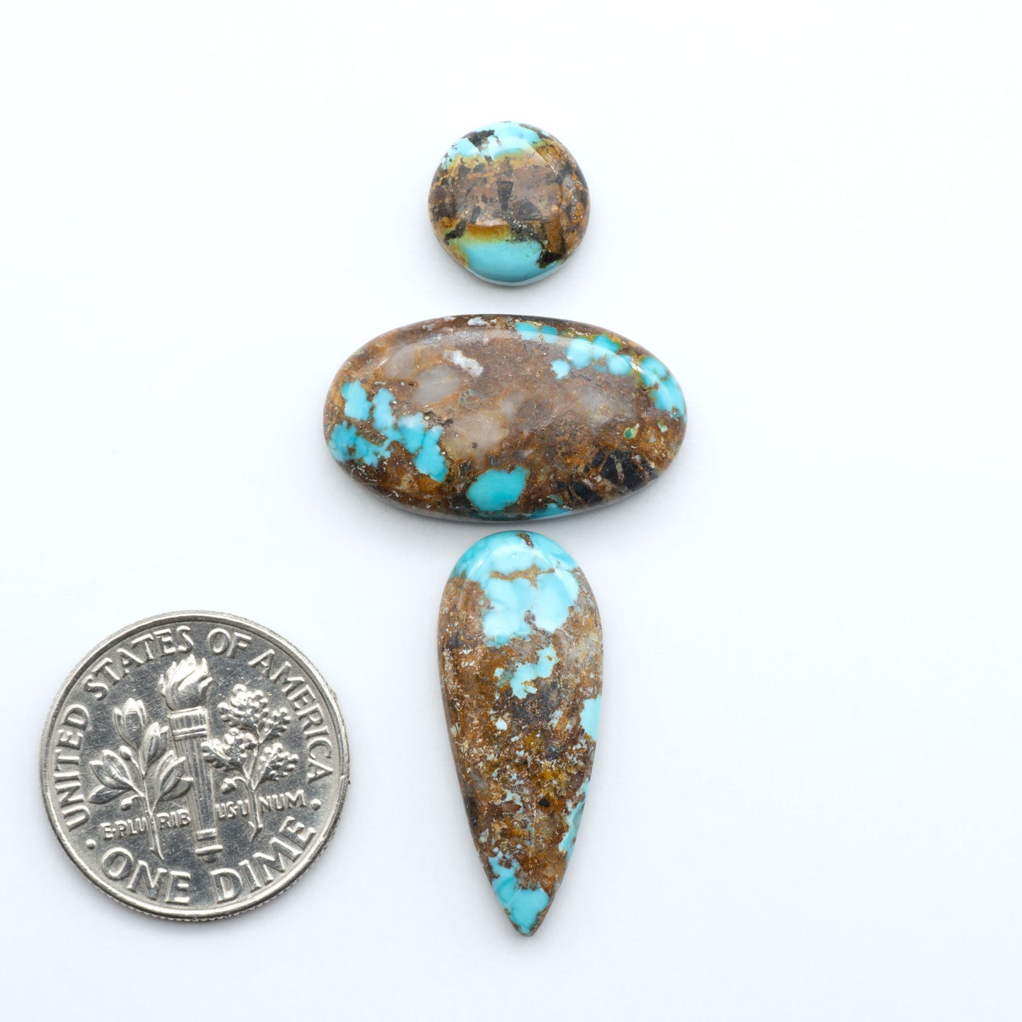Black Jack turquoise cabochons, blue-green color with black matrix, polished stones on a white background with a US dime for scale