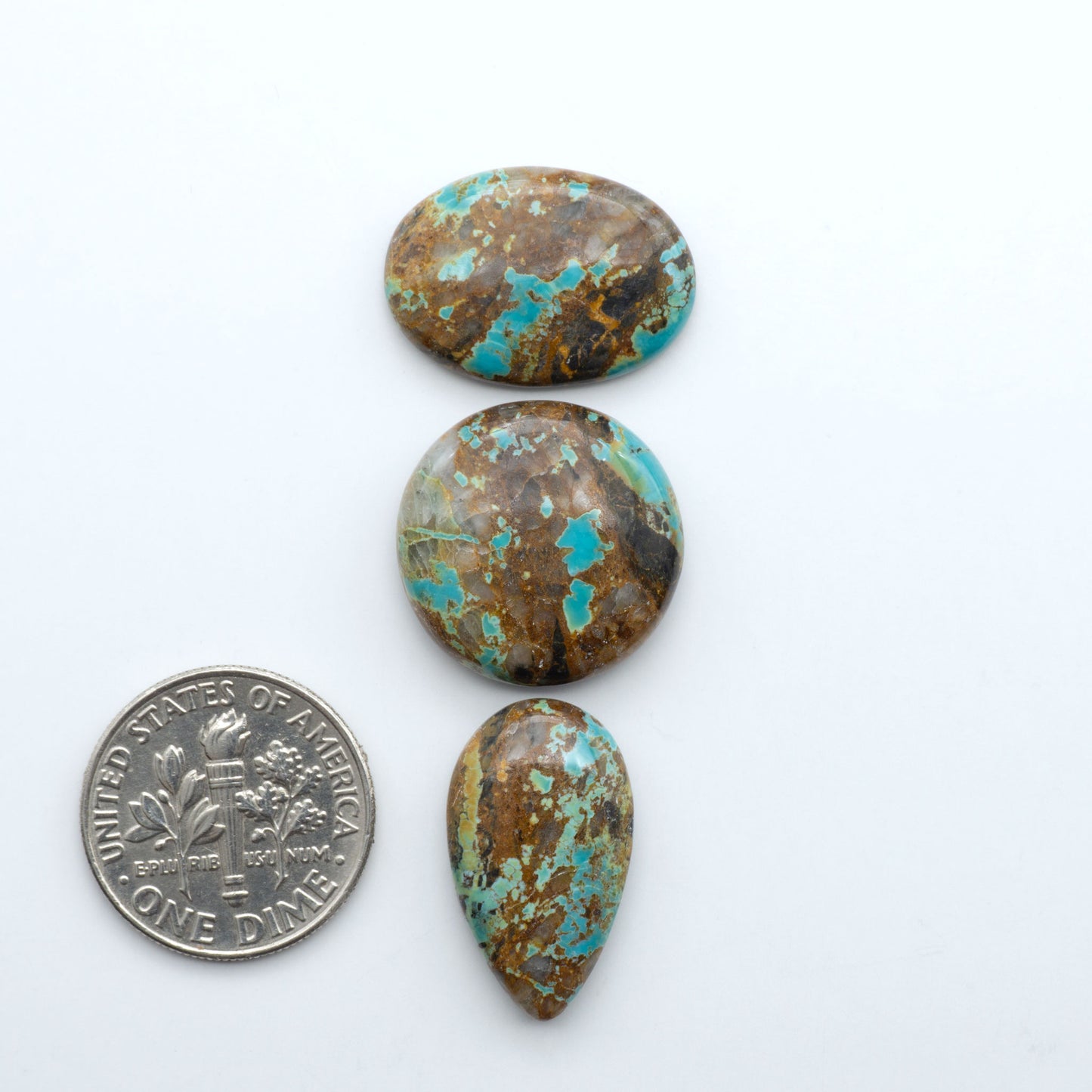 Black Jack turquoise cabochons, blue-green color with black matrix, polished stones on a white background with a US dime for scale