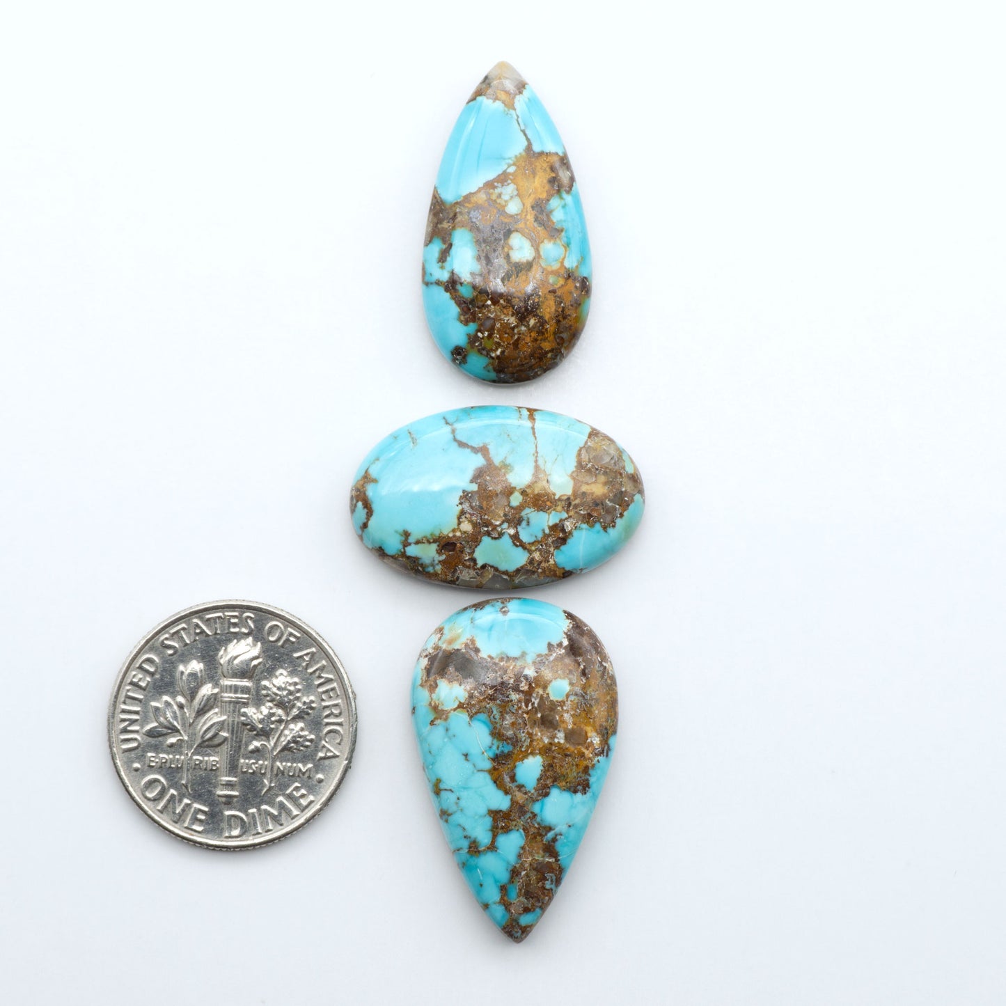 Black Jack turquoise cabochons, blue-green color with black matrix, polished stones on a white background with a US dime for scale