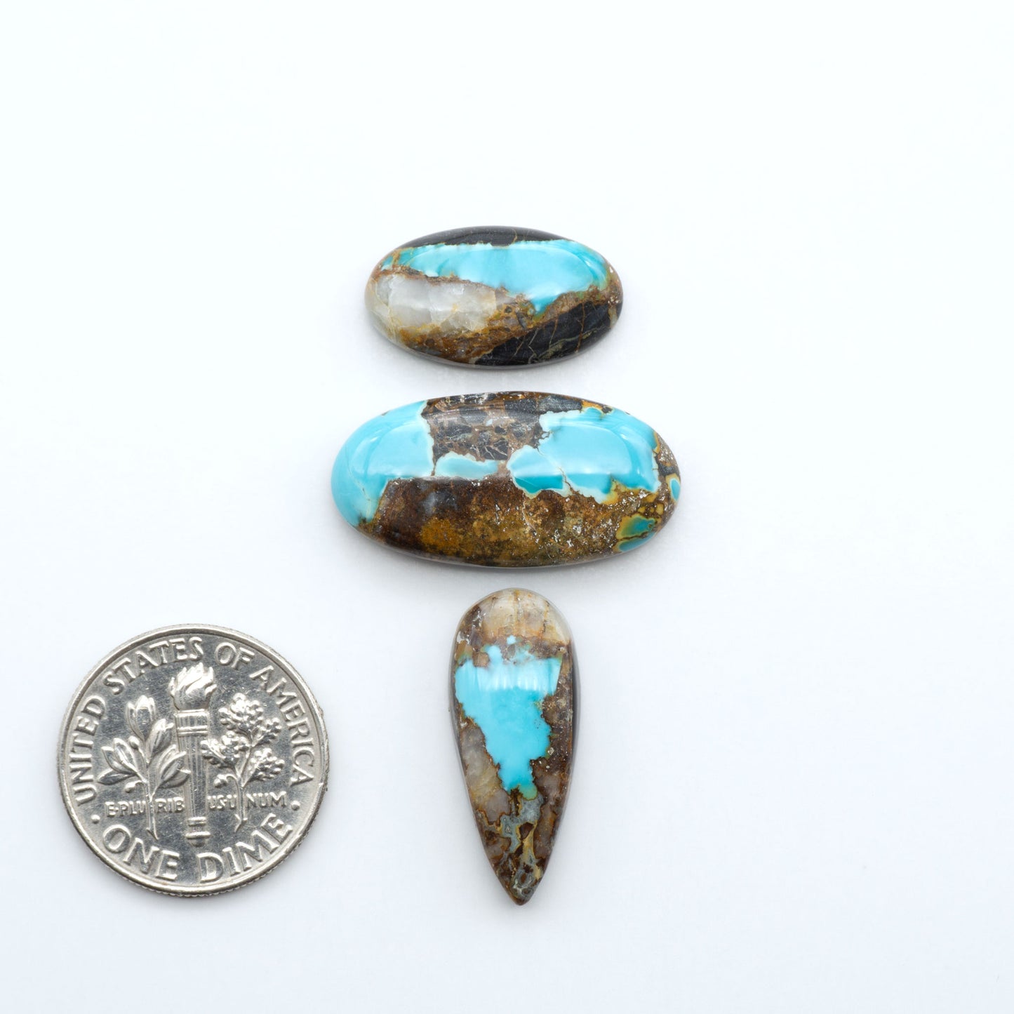 Black Jack turquoise cabochons, blue-green color with black matrix, polished stones on a white background with a US dime for scale