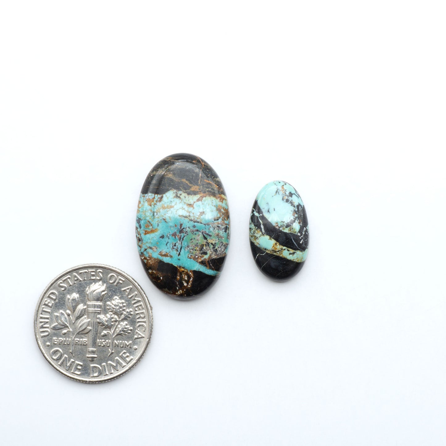 Black Jack turquoise cabochons, blue-green color with black matrix, polished stones on a white background with a US dime for scale