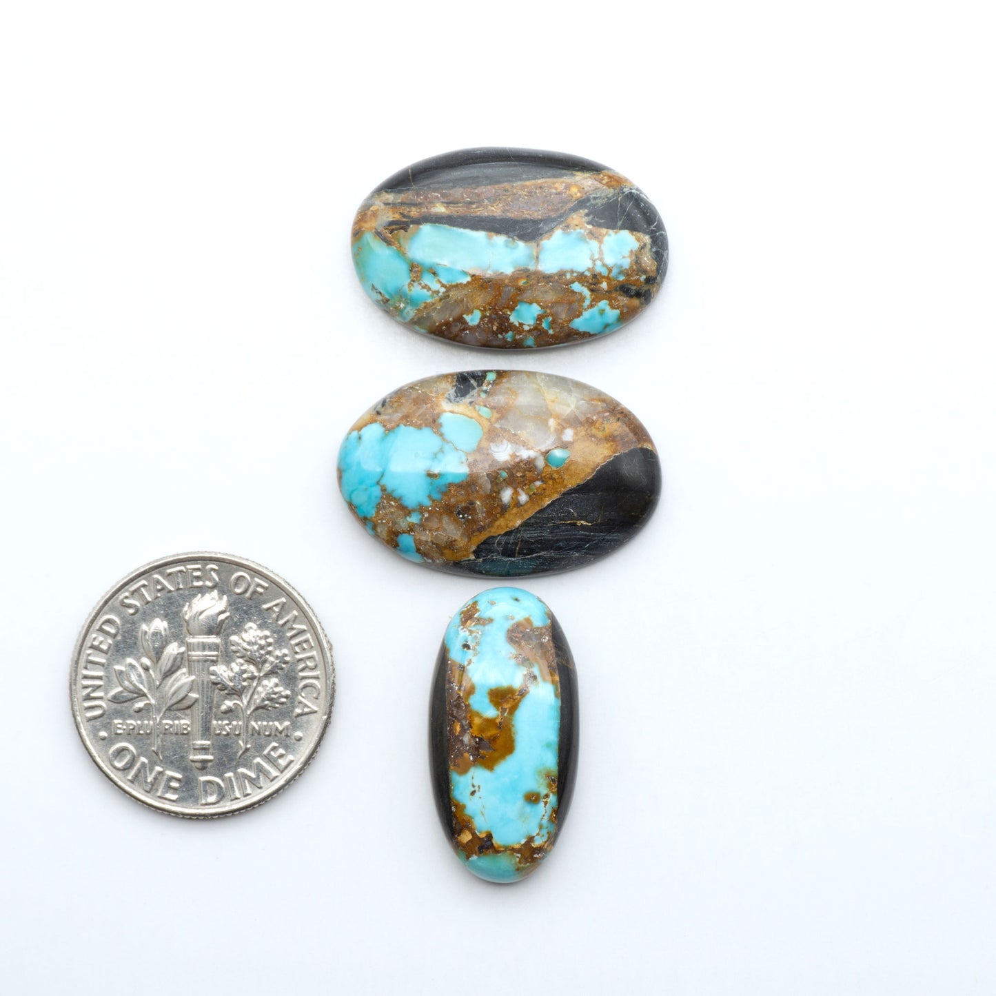 Black Jack turquoise cabochons, blue-green color with black matrix, polished stones on a white background with a US dime for scale