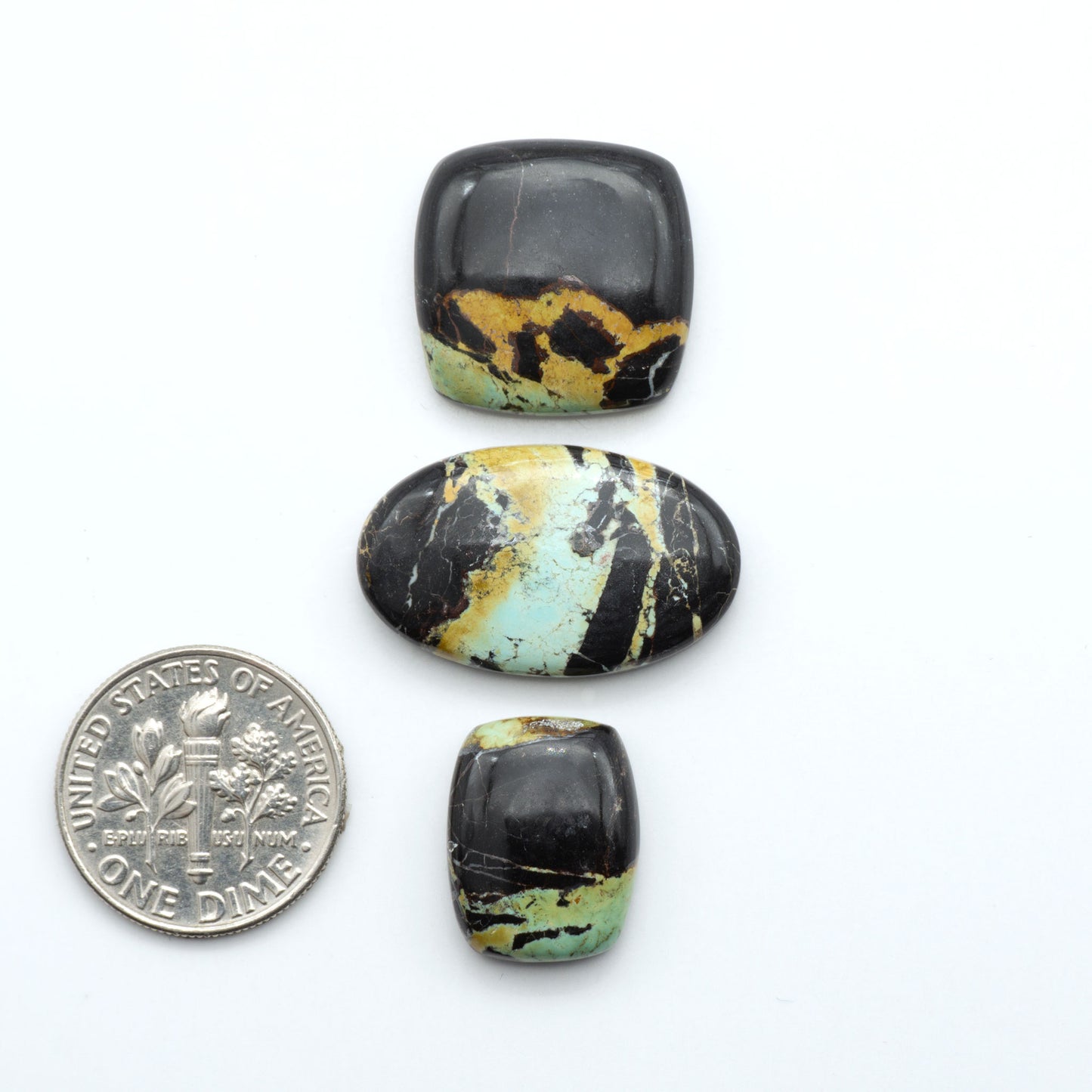 Black Jack turquoise cabochons, blue-green color with black matrix, polished stones on a white background with a US dime for scale