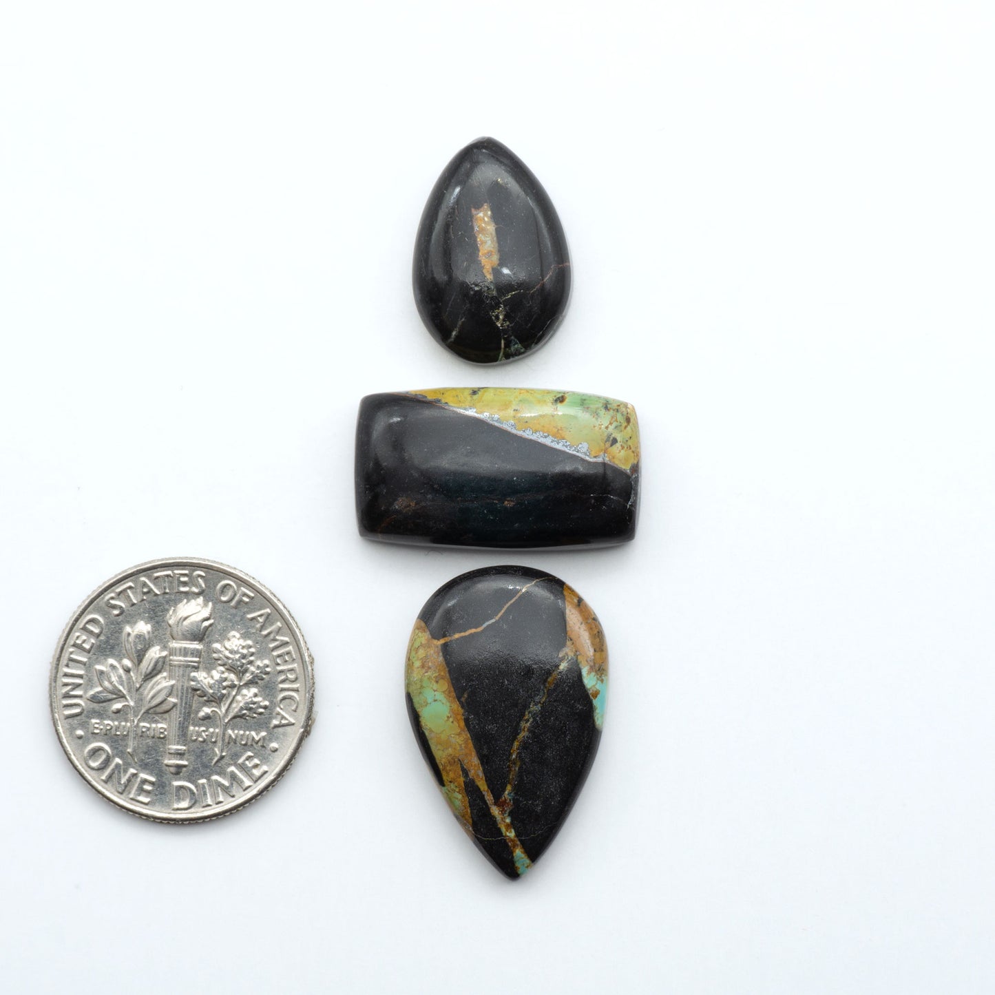 Black Jack turquoise cabochons, blue-green color with black matrix, polished stones on a white background with a US dime for scale