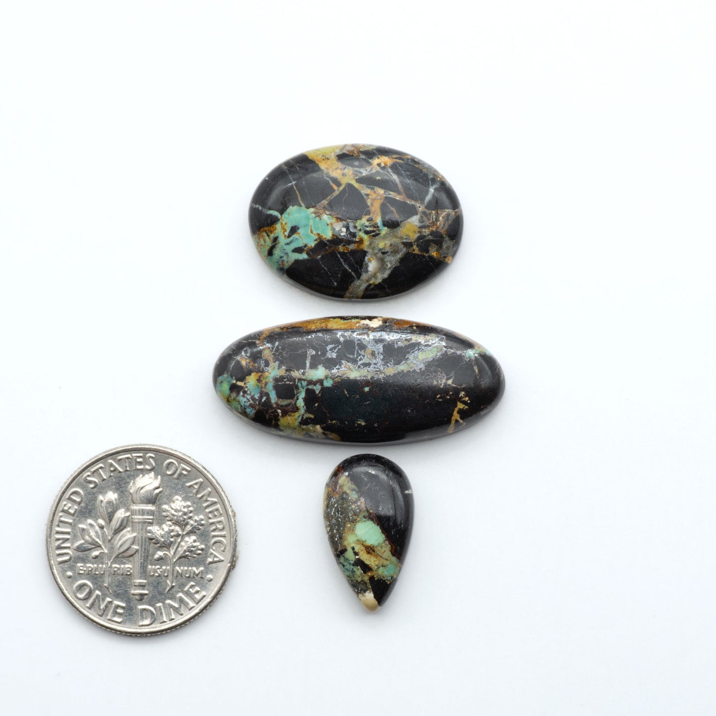Black Jack turquoise cabochons, blue-green color with black matrix, polished stones on a white background with a US dime for scale