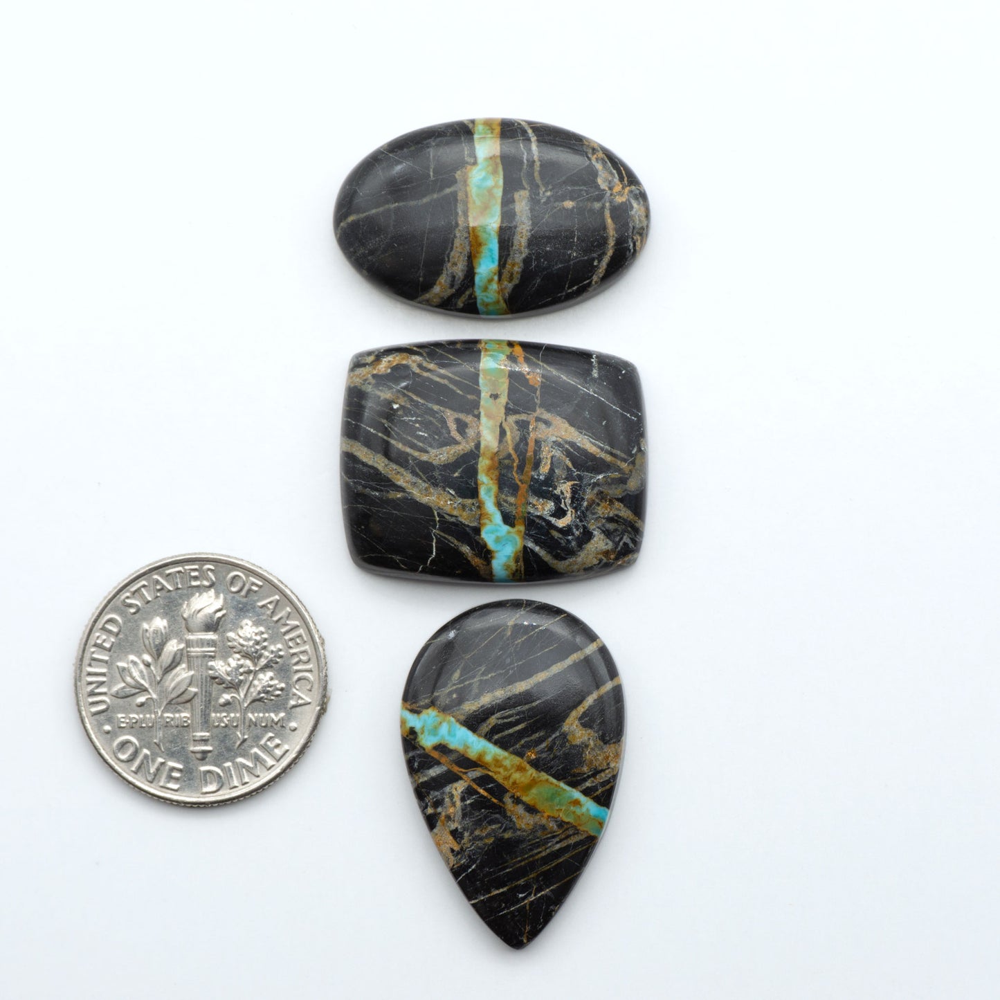 Black Jack turquoise cabochons, blue-green color with black matrix, polished stones on a white background with a US dime for scale