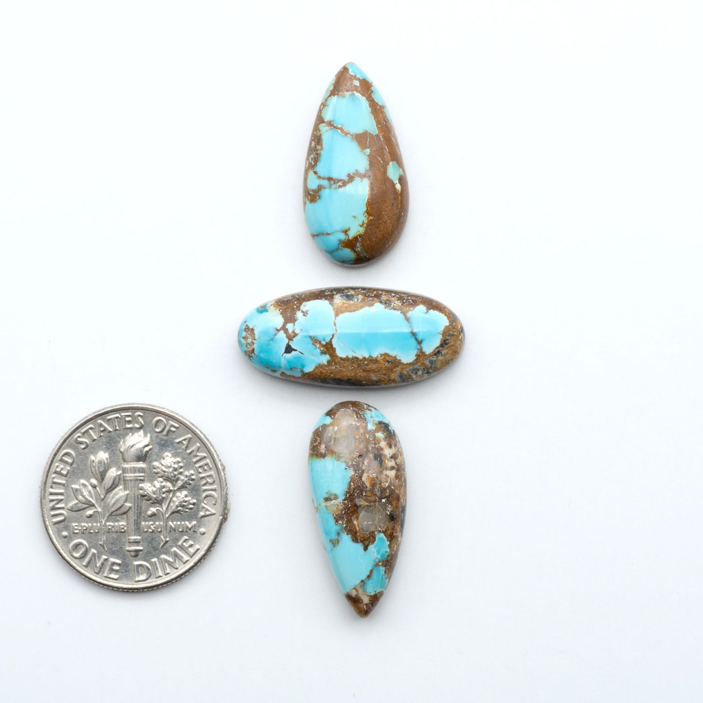 Black Jack turquoise cabochons, blue-green color with black matrix, polished stones on a white background with a US dime for scale