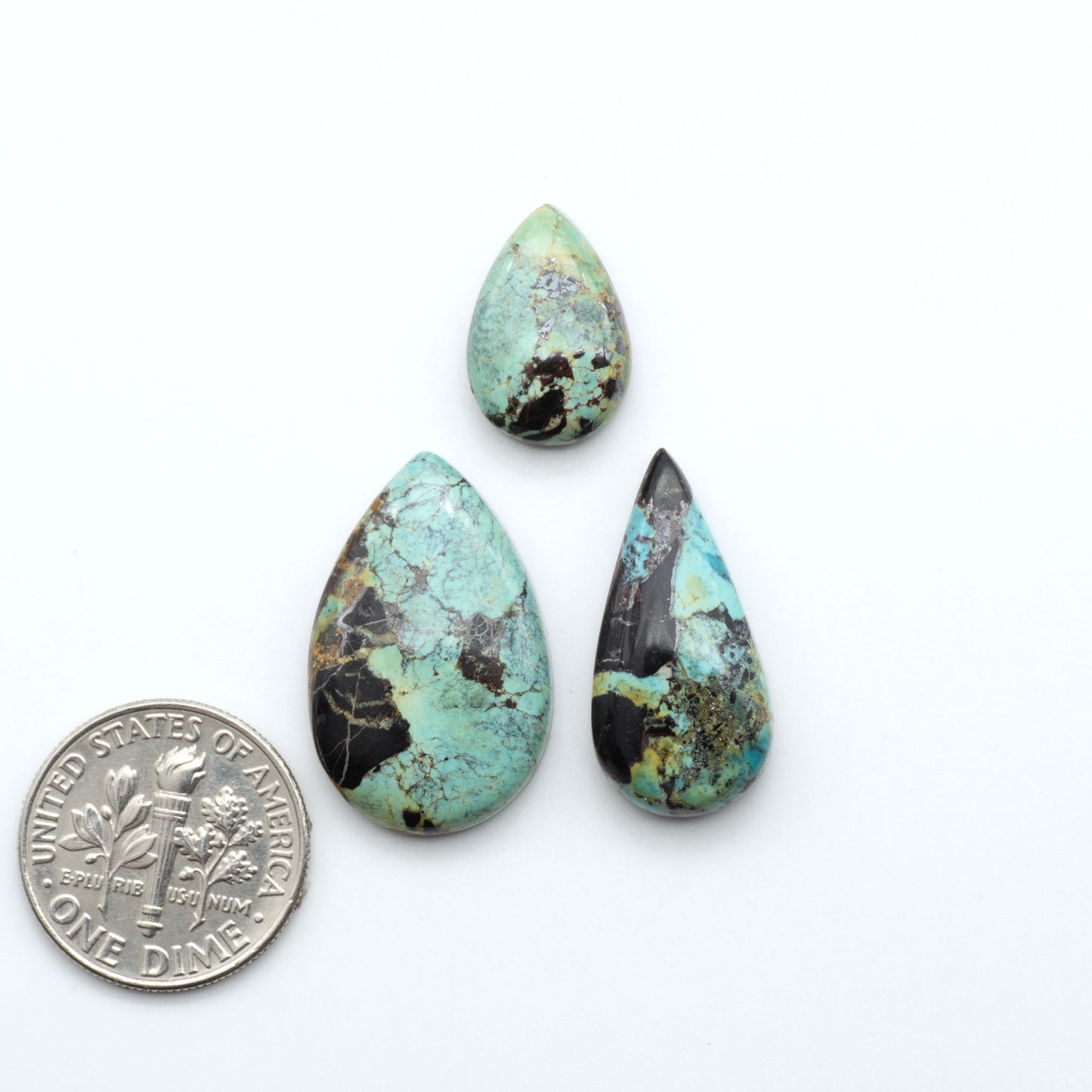 Black Jack turquoise cabochons, blue-green color with black matrix, polished stones on a white background with a US dime for scale