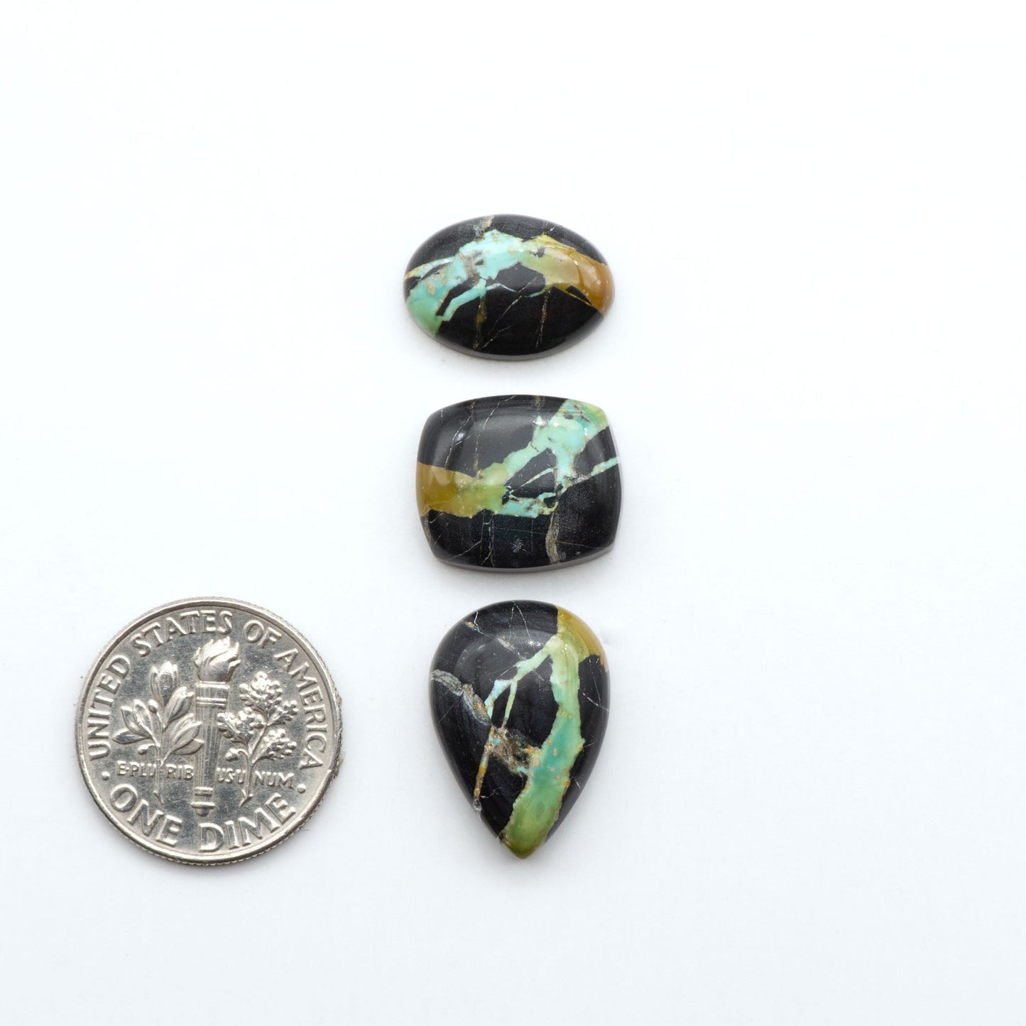 Black Jack turquoise cabochons, blue-green color with black matrix, polished stones on a white background with a US dime for scale