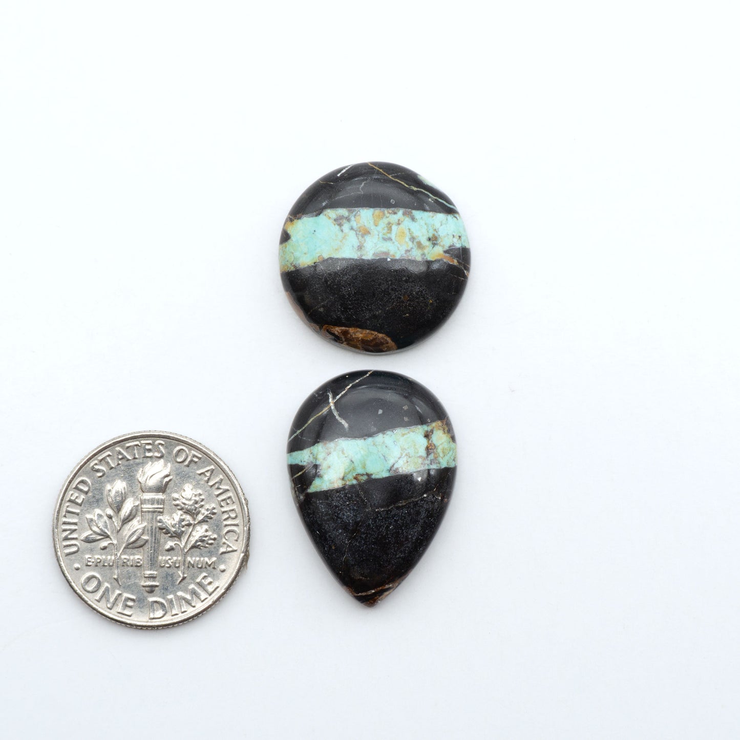 Black Jack turquoise cabochons, blue-green color with black matrix, polished stones on a white background with a US dime for scale