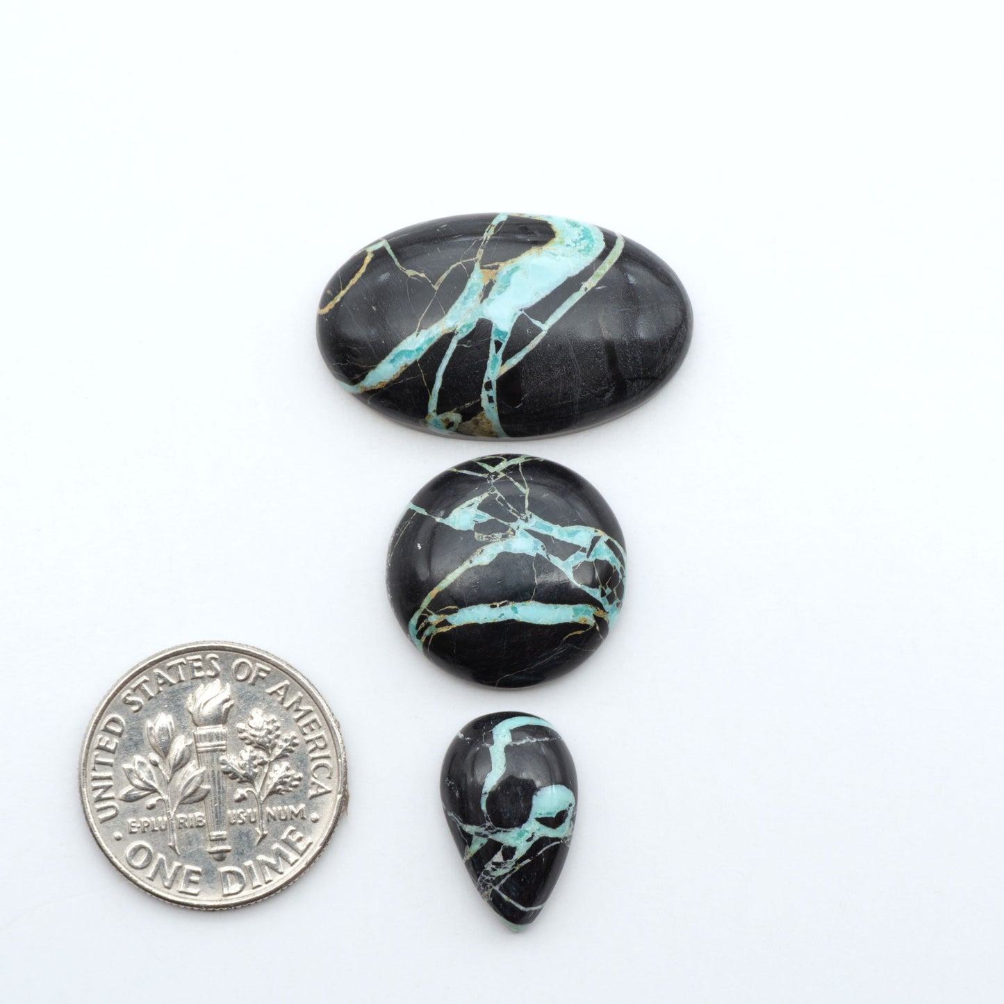 Black Jack turquoise cabochons, blue-green color with black matrix, polished stones on a white background with a US dime for scale