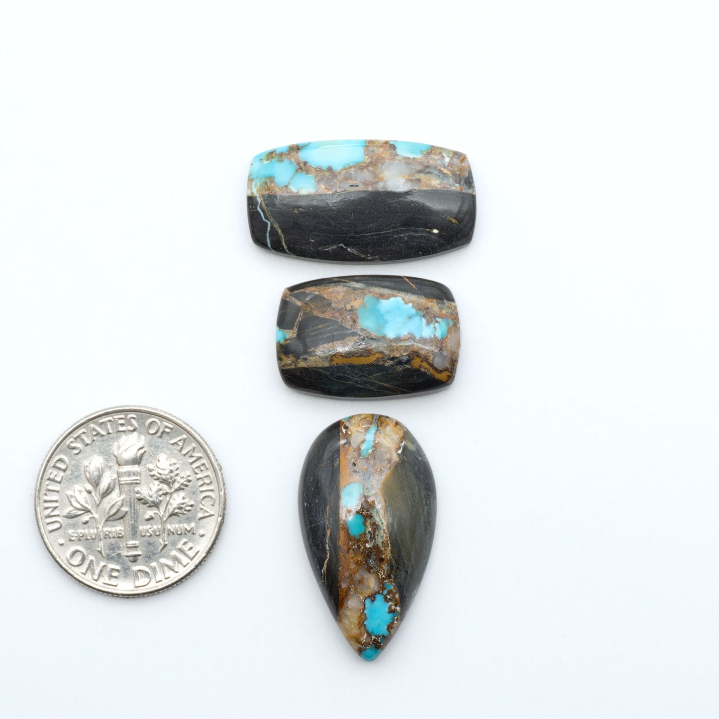 Black Jack turquoise cabochons, blue-green color with black matrix, polished stones on a white background with a US dime for scale