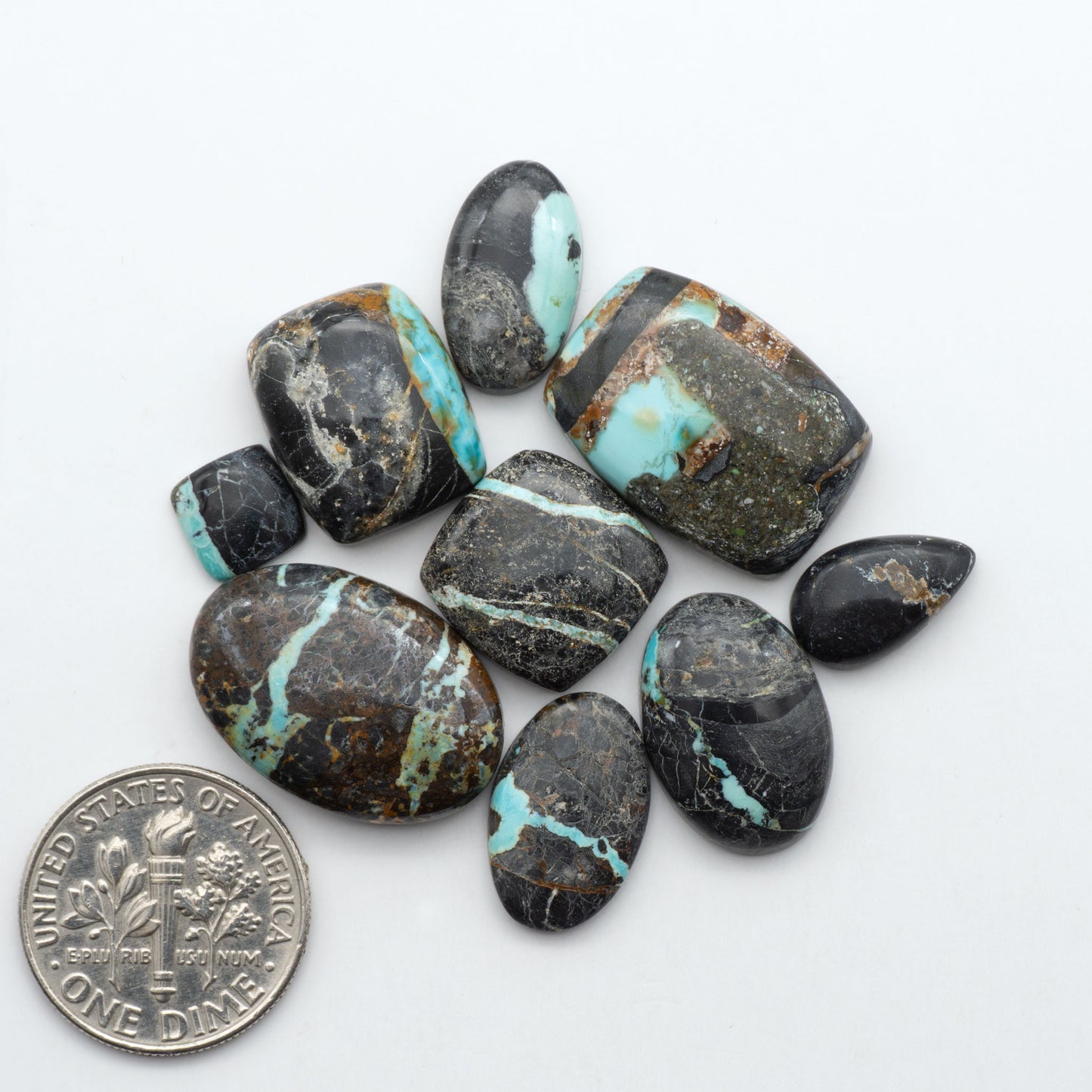 Black Jack turquoise cabochons, blue-green color with black matrix, polished stones on a white background with a US dime for scale