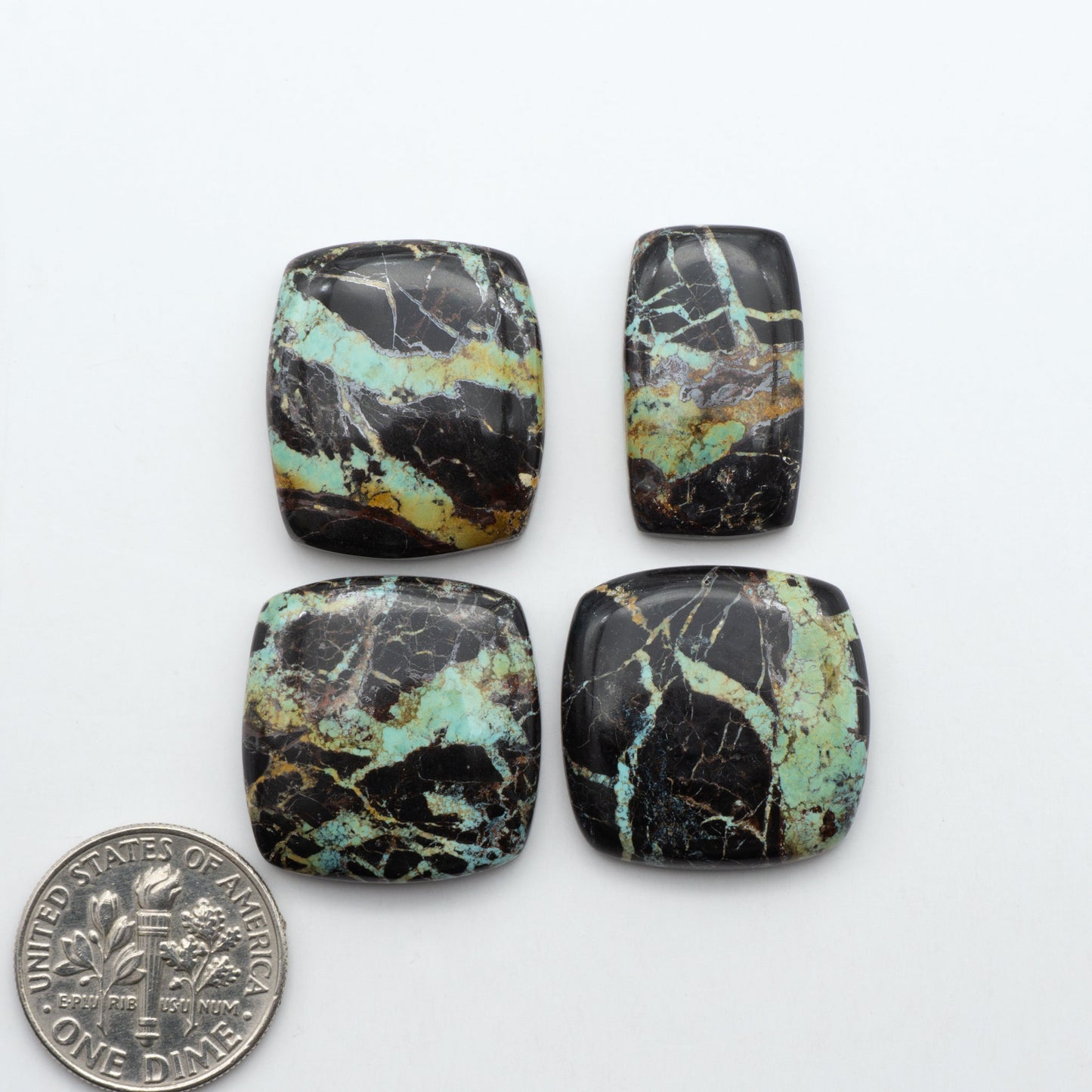 Black Jack turquoise cabochons, blue-green color with black matrix, polished stones on a white background with a US dime for scale