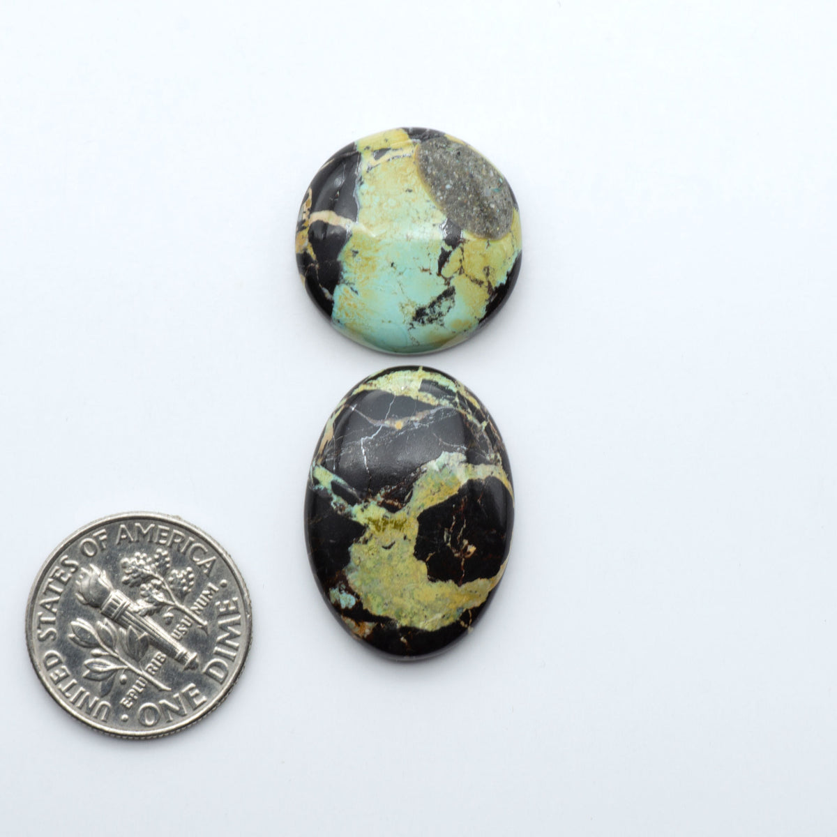 Black Jack turquoise cabochons, blue-green color with black matrix, polished stones on a white background with a US dime for scale
