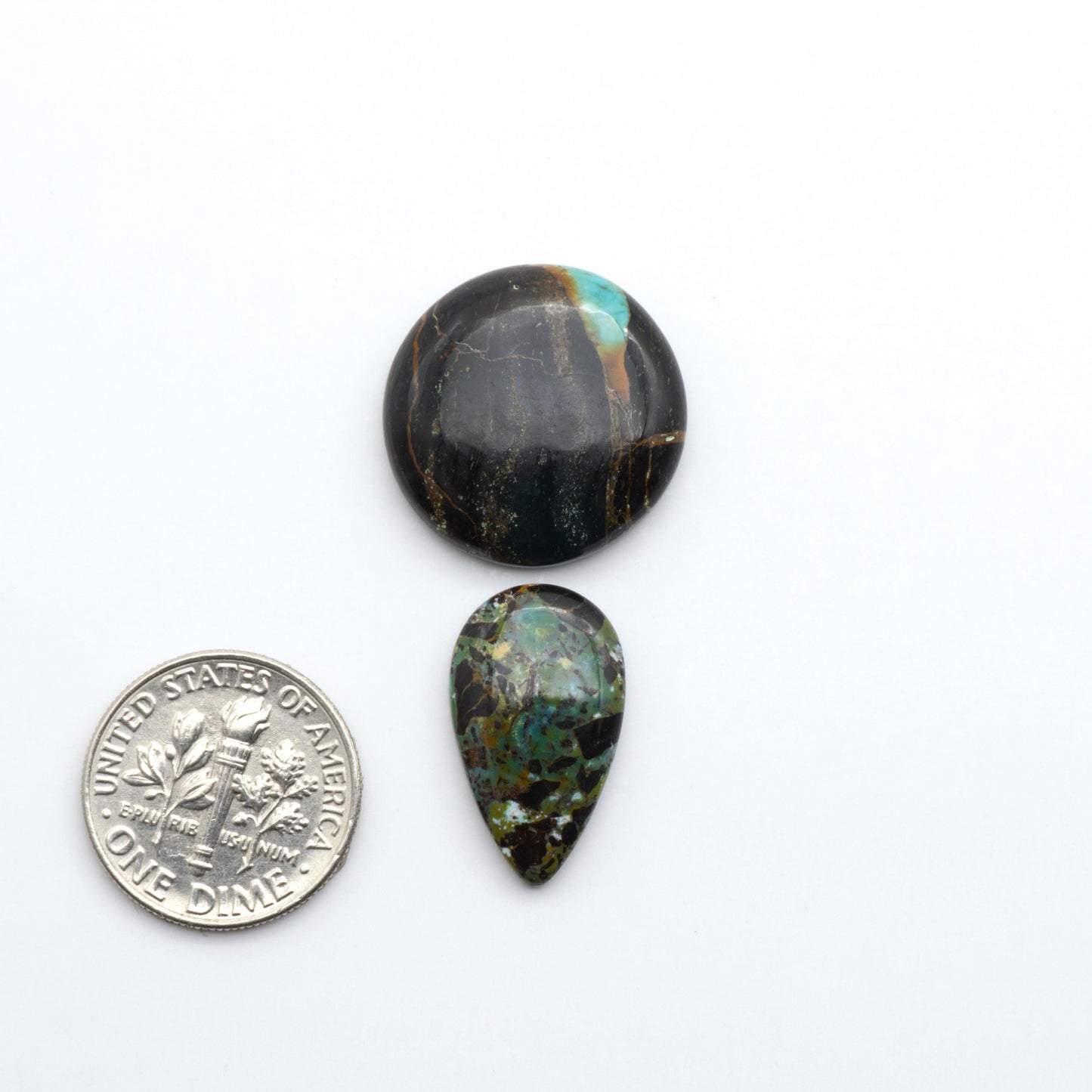 Two teardrop-shaped black & green turquoise cabochons on a white background with a dime for scale.