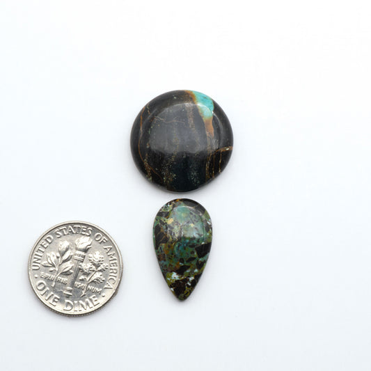 Two teardrop-shaped black & green turquoise cabochons on a white background with a dime for scale.