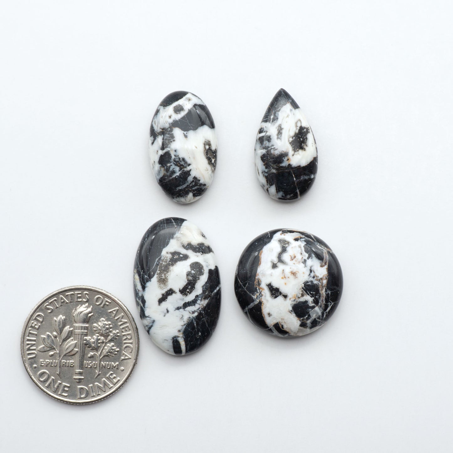 Four black and white marbled stones with a dime for scale on a white background.Natural White Buffalo Stone Cabochons are semi-precious gemstones cut into shapes ideal for jewelry-making, making them an excellent choice for artisans.