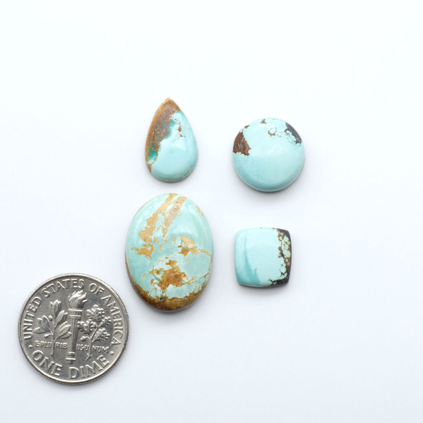 Turquoise stones with gold veins on a white background, one coin for scale. Number 8 Turquoise Cabochons have been selected for their quality and unique appearance. Don't miss the chance to add a one-of-a-kind piece to your collection.