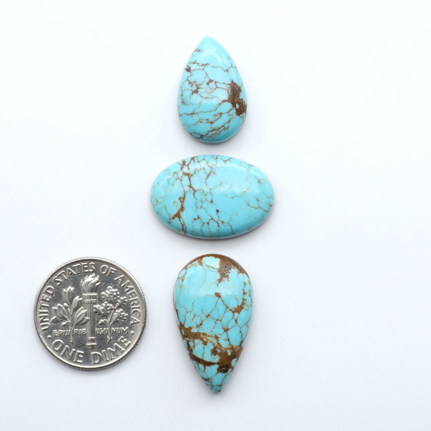 Three turquoise teardrop-shaped stones with a dime for scale on a white background. Number 8 Turquoise Cabochons have been selected for their quality and unique appearance. Don't miss the chance to add a one-of-a-kind piece to your collection.