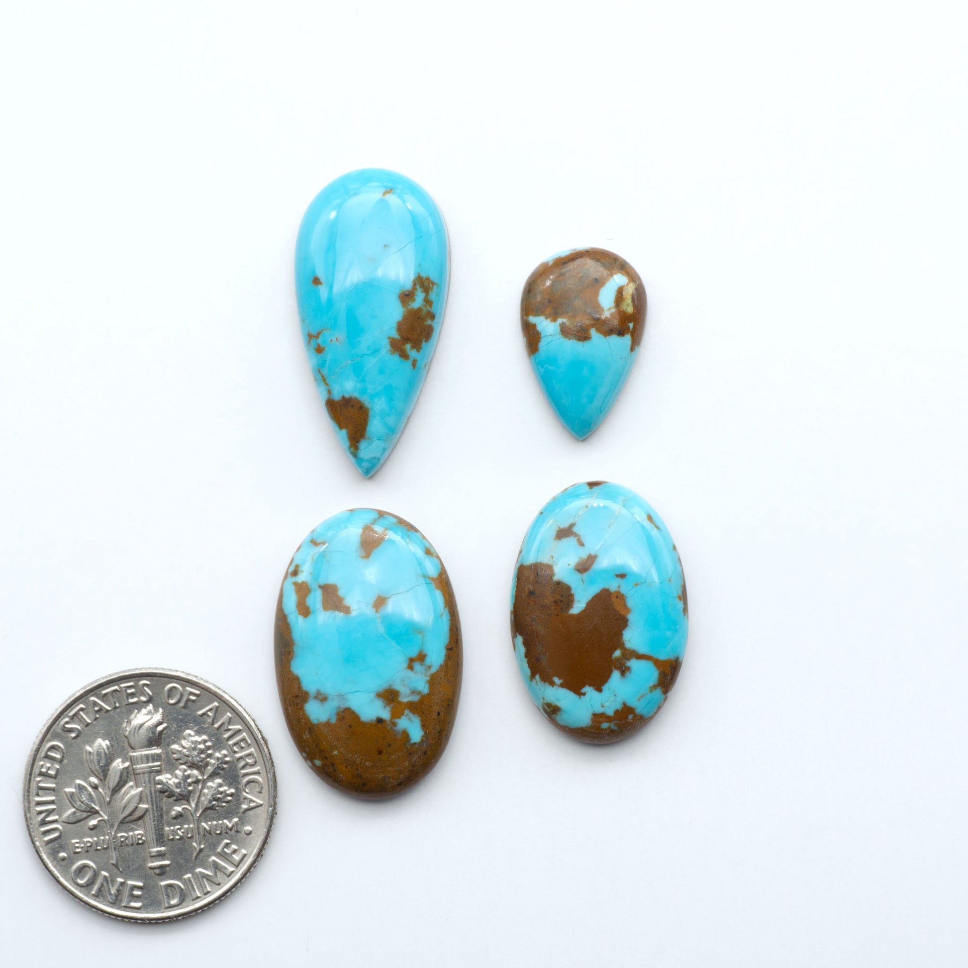 Turquoise stones with brown spots on a white background, one coin for scale. Number 8 Turquoise Cabochons have been selected for their quality and unique appearance. Don't miss the chance to add a one-of-a-kind piece to your collection.