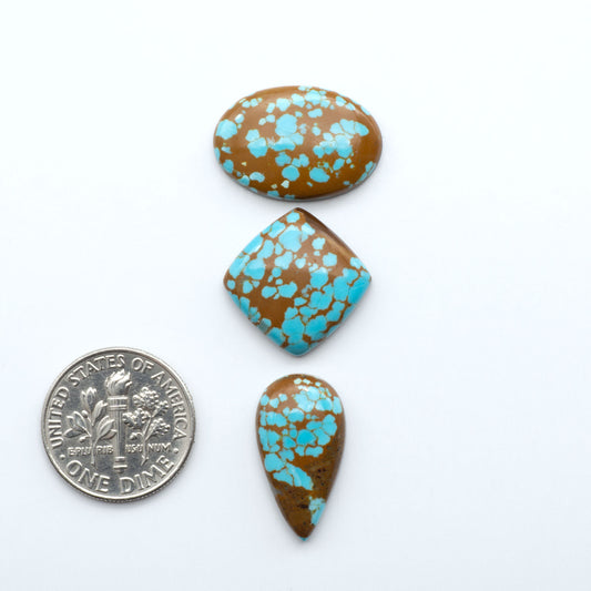 Three turquoise and brown speckled stones with a U.S. quarter for scale on a white background. Number 8 Turquoise Cabochons have been selected for their quality and unique appearance. Don't miss the chance to add a one-of-a-kind piece to your collection.