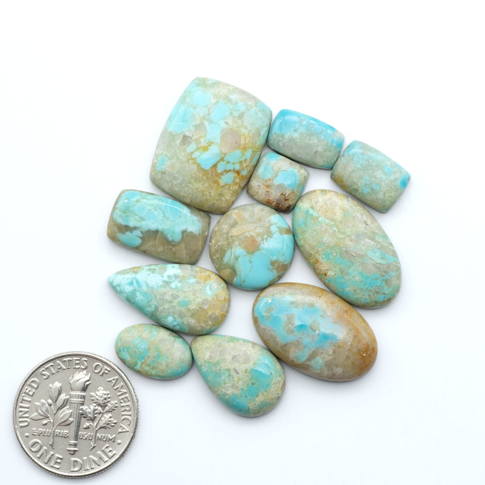 Turquoise stones with a U.S. dime for scale on a white background. Add a touch of beauty to your collection with our stunning Pilot Mountain Turquoise Cabochons. Perfect for jewelry making each piece is truly one-of-a-kind.