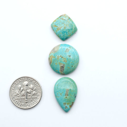 Turquoise stones with a U.S. dime for scale on a white background. Experience the beauty of Turquoise Mountain Cabochons. With their distinctive blue and green color, these gemstones are perfect for any jewelry piece.
