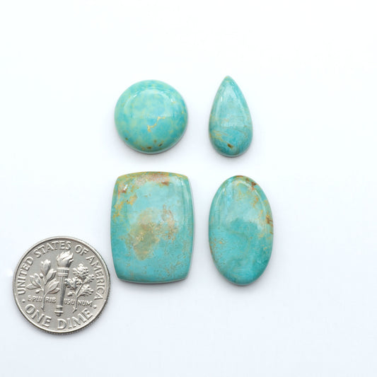 Turquoise stones with a U.S. dime for scale on a white background. Experience the beauty of Turquoise Mountain Cabochons. With their distinctive blue and green color, these gemstones are perfect for any jewelry piece.