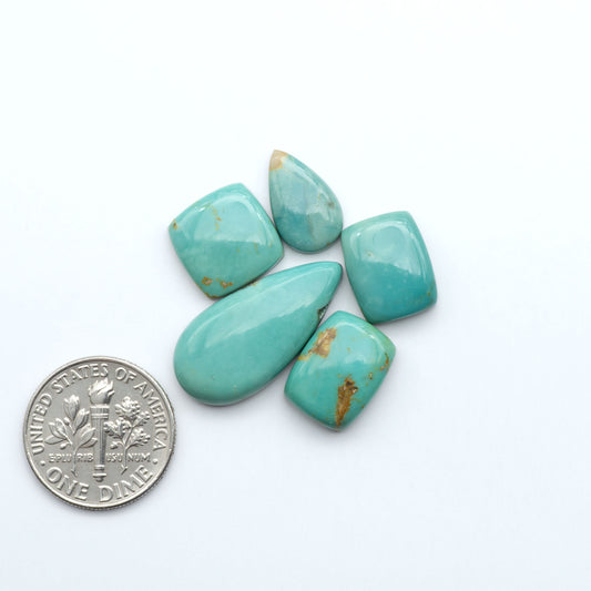 Turquoise stones with a U.S. dime for scale on a white background. Experience the beauty of Turquoise Mountain Cabochons. With their distinctive blue and green color, these gemstones are perfect for any jewelry piece.