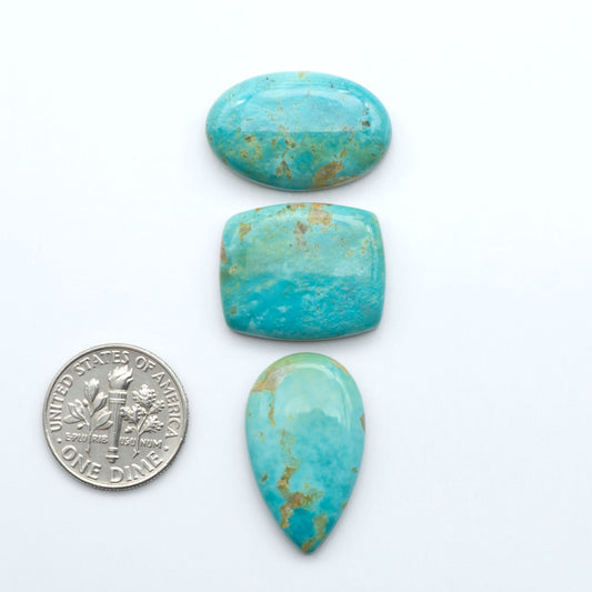 Turquoise stones with a U.S. dime for scale on a white background. Experience the beauty of Turquoise Mountain Cabochons. With their distinctive blue and green color, these gemstones are perfect for any jewelry piece.