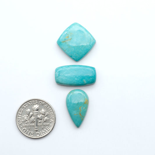Turquoise stones with a U.S. dime for scale on a white background. Experience the beauty of Turquoise Mountain Cabochons. With their distinctive blue and green color, these gemstones are perfect for any jewelry piece.