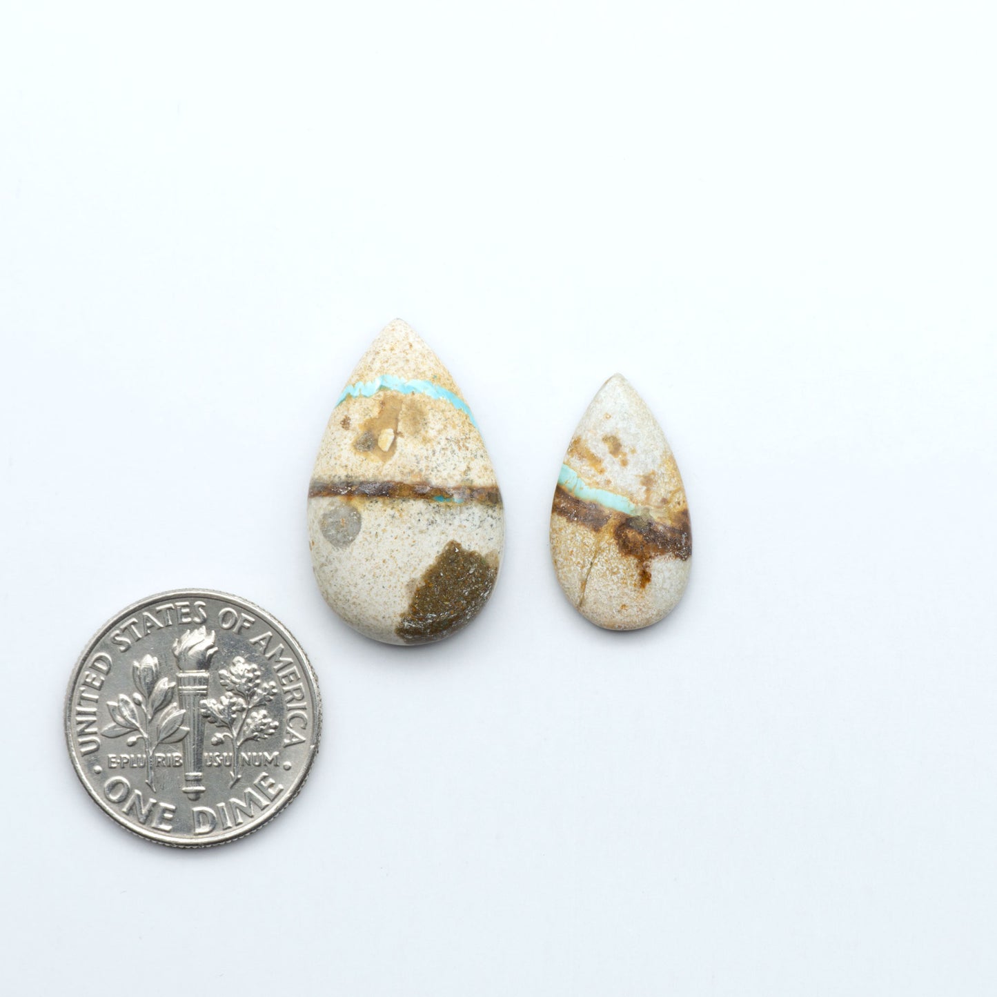 Two teardrop-shaped stones with a coin for scale on a white background. Royston Turquoise cabochons are famous for their distinctive matrix and unique green and blue hues, making them a favored option among jewelry designers.