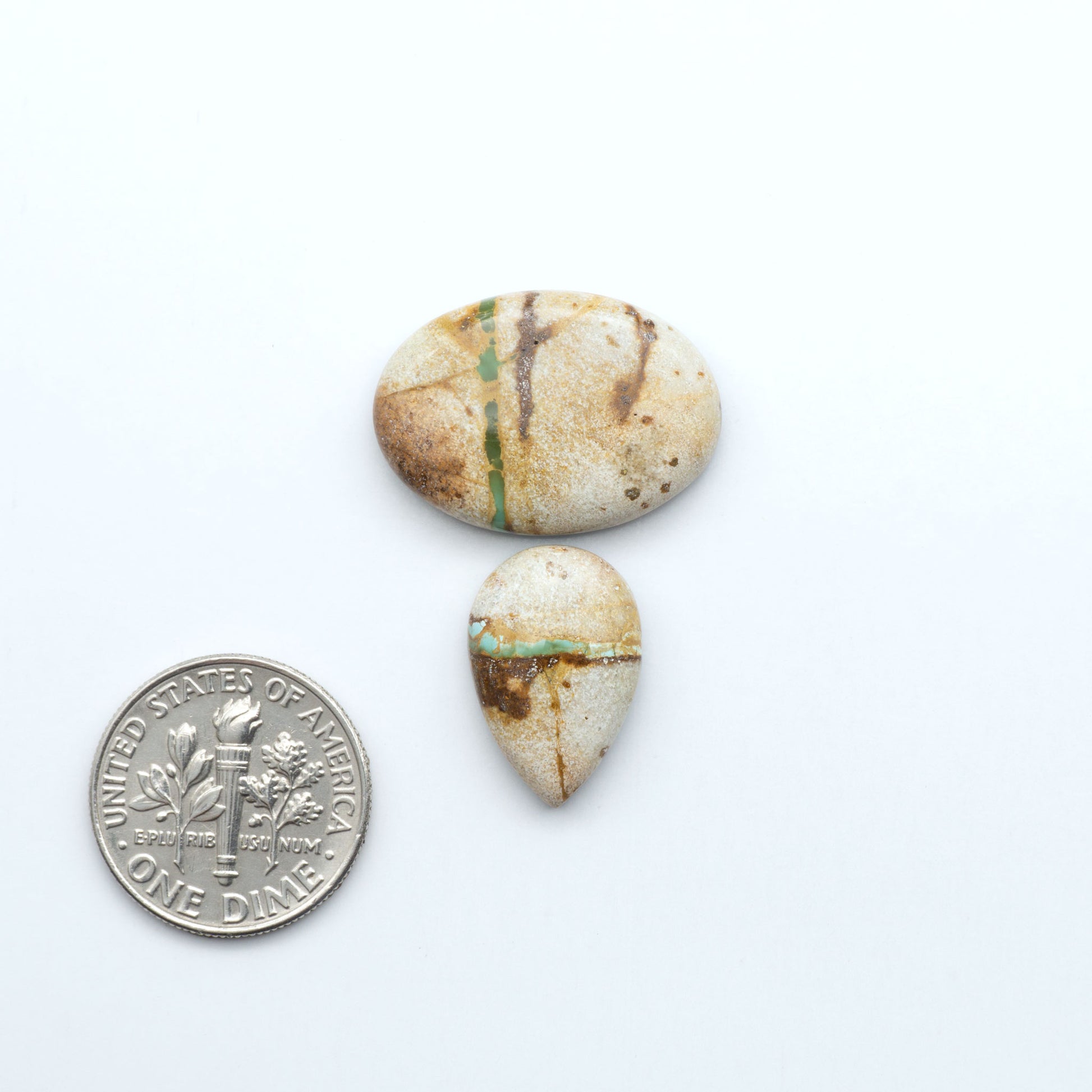 Two stones with natural patterns next to a U.S. dime on a white background. Royston Turquoise cabochons are famous for their distinctive matrix and unique green and blue hues, making them a favored option among jewelry designers.