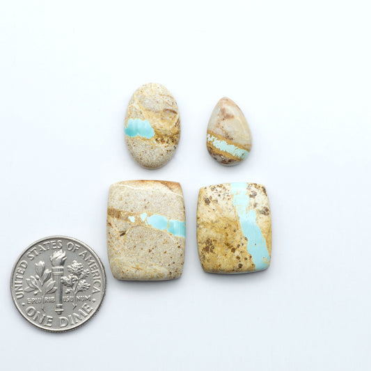 Four stone beads with turquoise inclusions next to a U.S. quarter dollar on a white background. Royston Turquoise cabochons are famous for their distinctive matrix and unique green and blue hues, making them a favored option among jewelry designers.