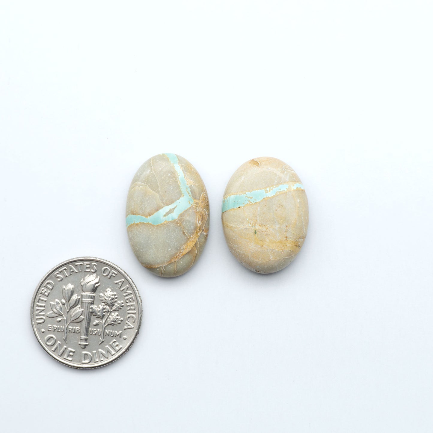 Two oval stones with turquoise stripes next to a U.S. dime on a white background. Royston Turquoise cabochons are famous for their distinctive matrix and unique green and blue hues, making them a favored option among jewelry designers.