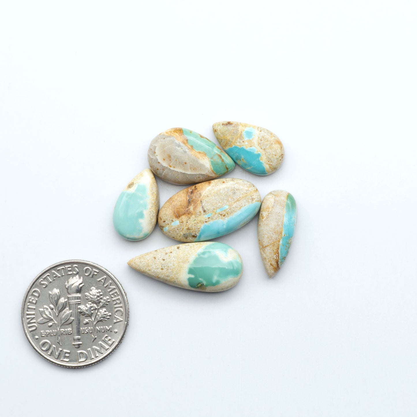 Turquoise and beige stones on a white background with a silver dime for scale. Royston Turquoise cabochons are famous for their distinctive matrix and unique green and blue hues, making them a favored option among jewelry designers.