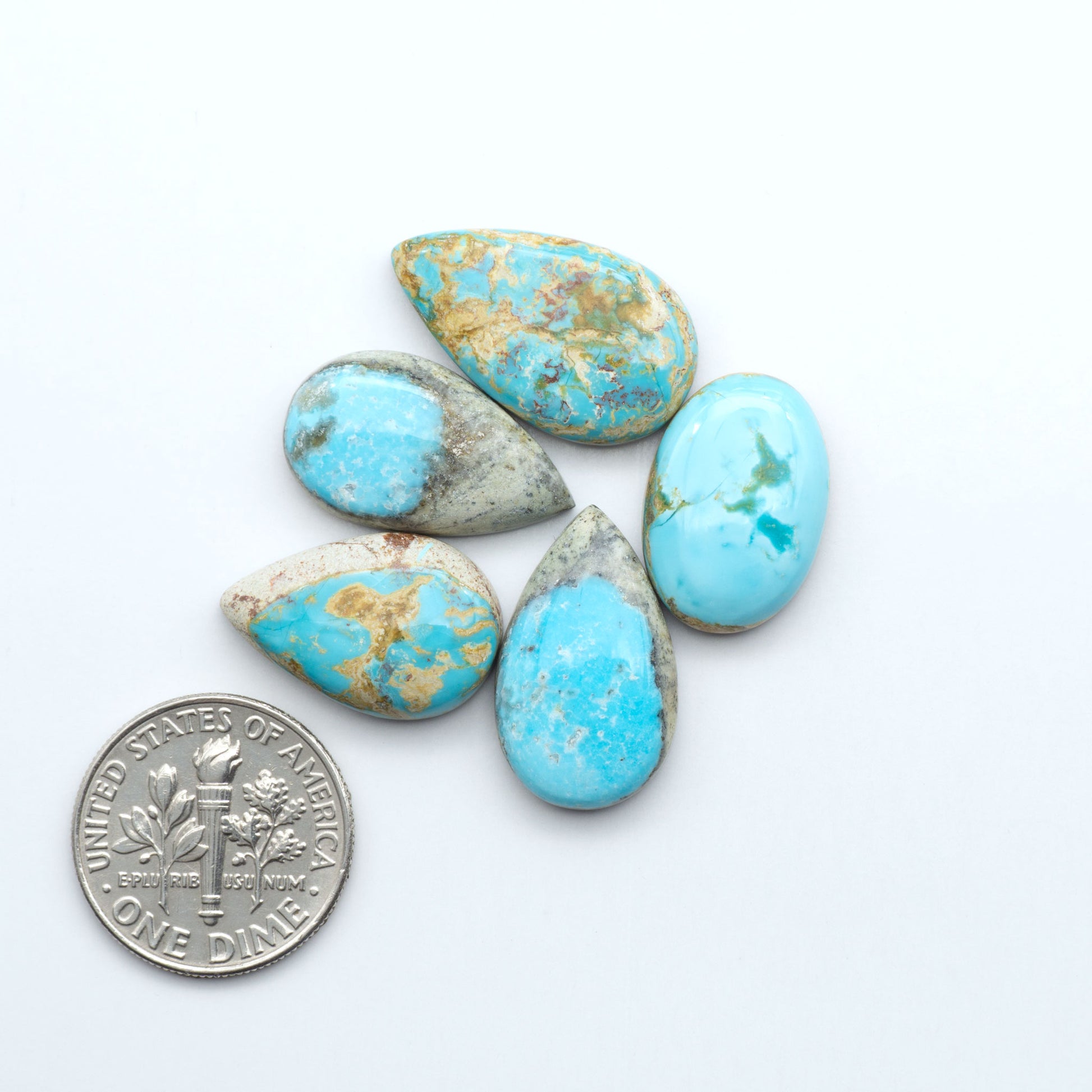 Five turquoise stones of varying sizes on a white background with a dime for scale. Royston Turquoise cabochons are famous for their distinctive matrix and unique green and blue hues, making them a favored option among jewelry designers.