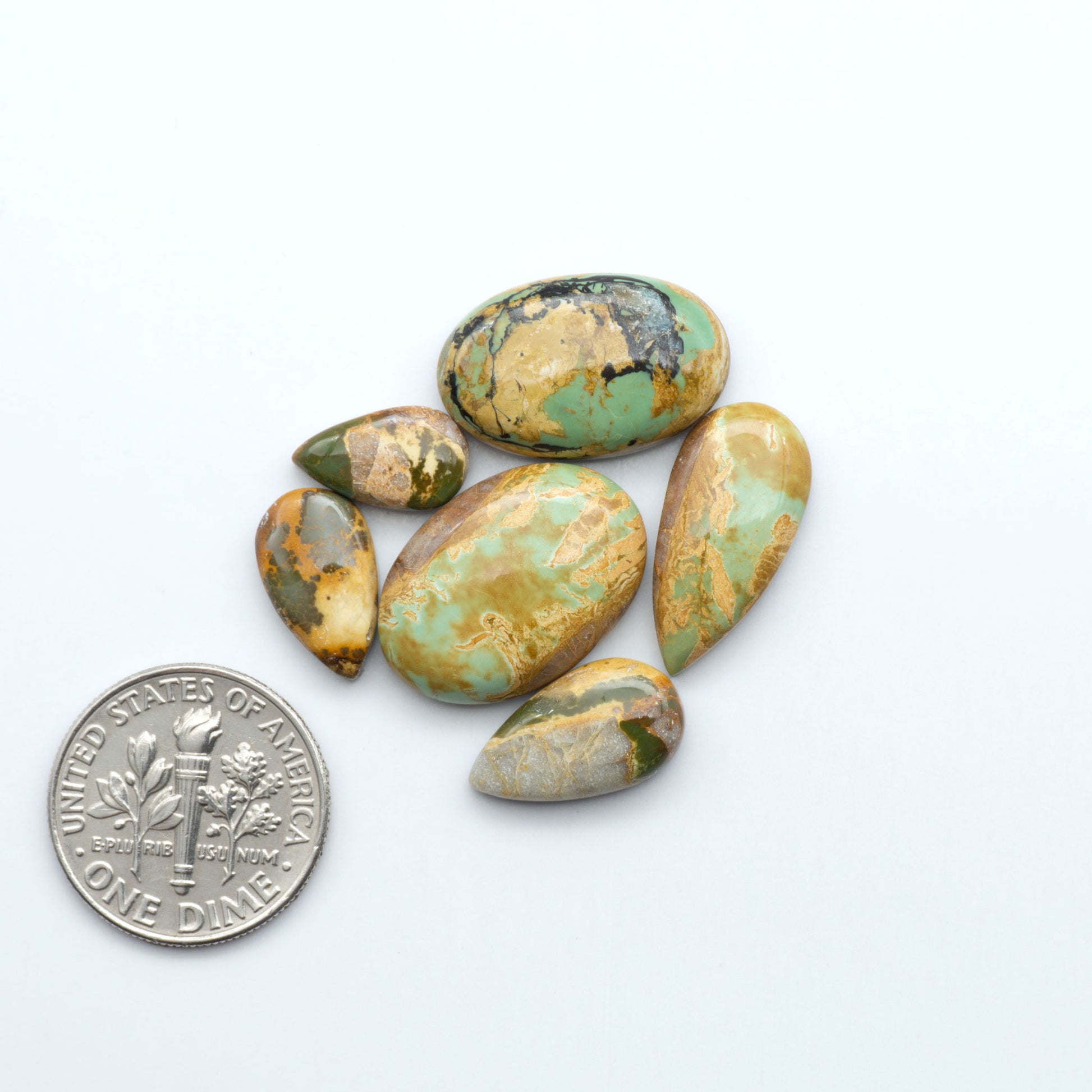 Turquoise stones with a dime for scale on a white background. Royston Turquoise cabochons are famous for their distinctive matrix and unique green and blue hues, making them a favored option among jewelry designers.
