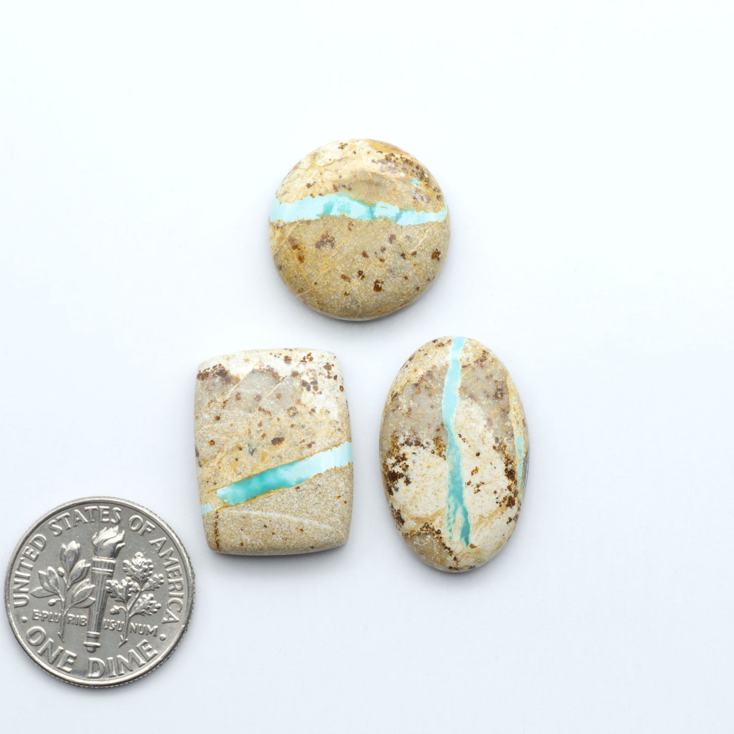 Three stones with turquoise inlay next to a U.S. dime on a white background. Royston Turquoise cabochons are famous for their distinctive matrix and unique green and blue hues, making them a favored option among jewelry designers.