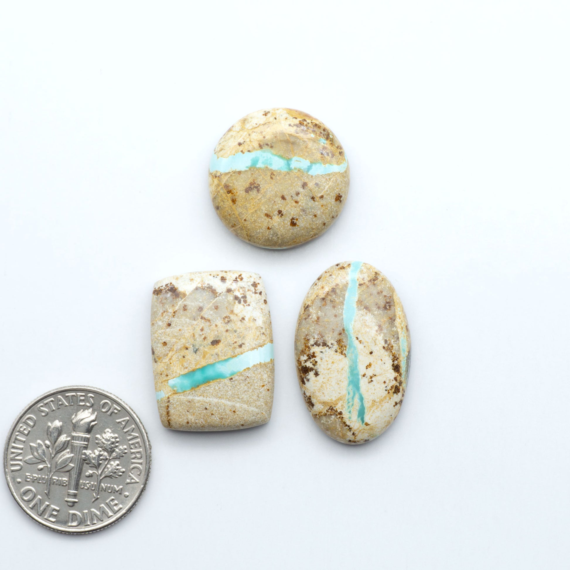 Three stones with turquoise inlay next to a U.S. dime on a white background. Royston Turquoise cabochons are famous for their distinctive matrix and unique green and blue hues, making them a favored option among jewelry designers.