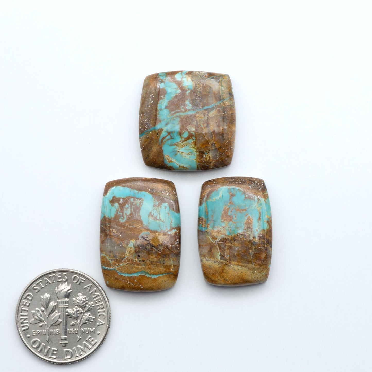 Three rectangular turquoise stones with a U.S. dime coin for size comparison on a white background. Royston Turquoise cabochons are famous for their distinctive matrix and unique green and blue hues, making them a favored option among jewelry designers.
