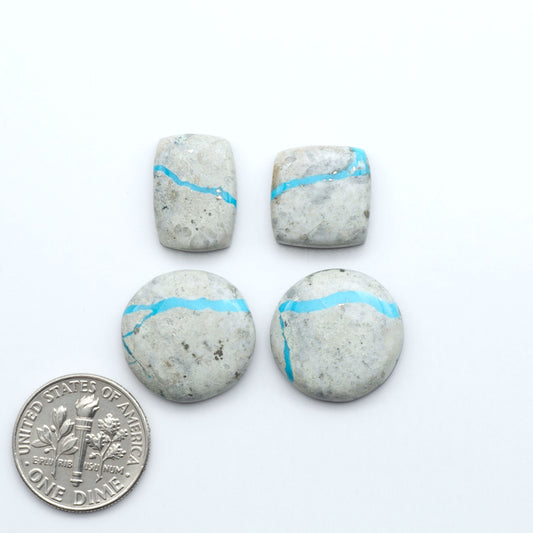 Four stones with blue veins on a white background, one quarter coin for scale. Royston Turquoise cabochons are famous for their distinctive matrix and unique green and blue hues, making them a favored option among jewelry designers.