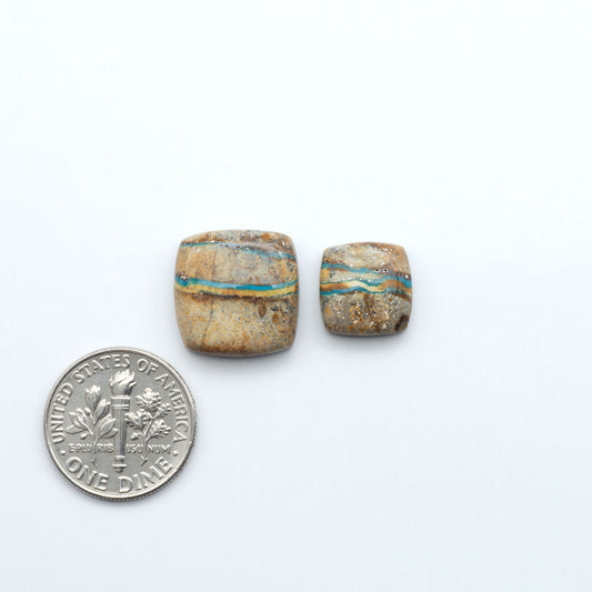Two stone beads next to a U.S. dime on a white background. Royston Turquoise cabochons are famous for their distinctive matrix and unique green and blue hues, making them a favored option among jewelry designers.