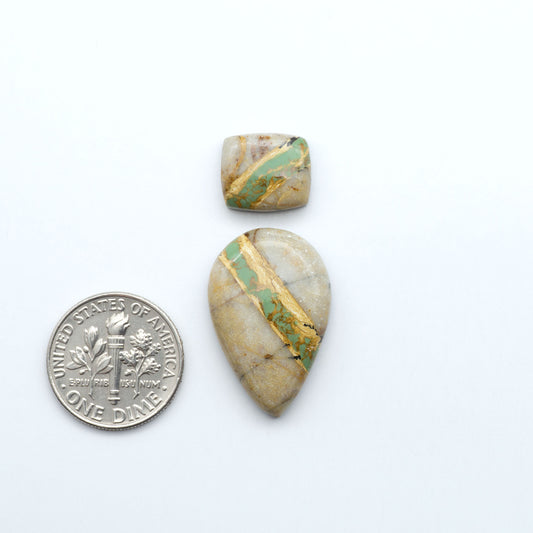 Two stone pendants with gold and green inlay on a white background, one next to a dime for scale. Royston Turquoise cabochons are famous for their distinctive matrix and unique green and blue hues, making them a favored option among jewelry designers.